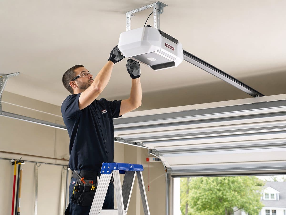 Technician on a ladder installing a ceiling-mounted garage door opener and rail
